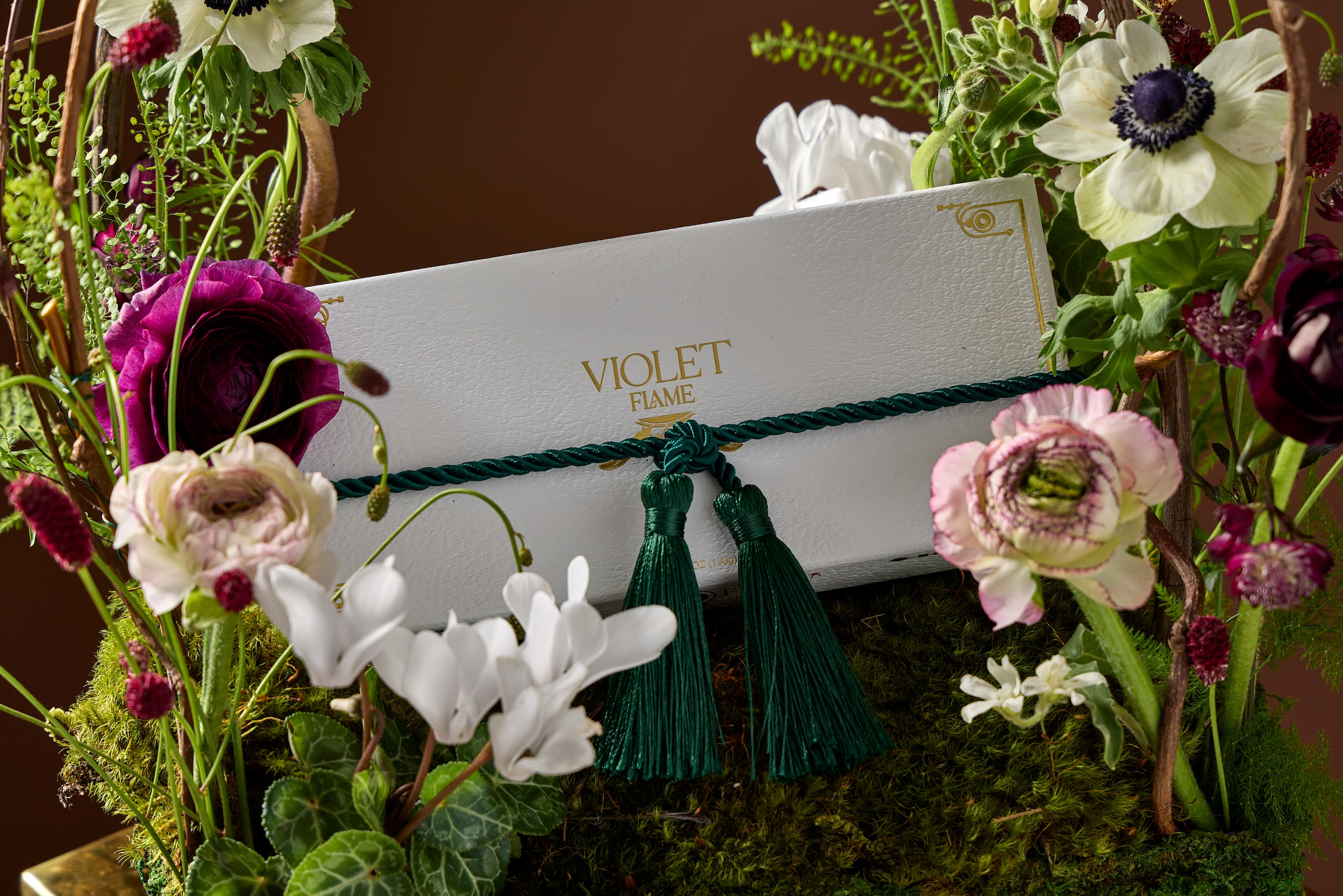 Beautiful gift box of chocolate truffles tied with green tassel situated among flowers