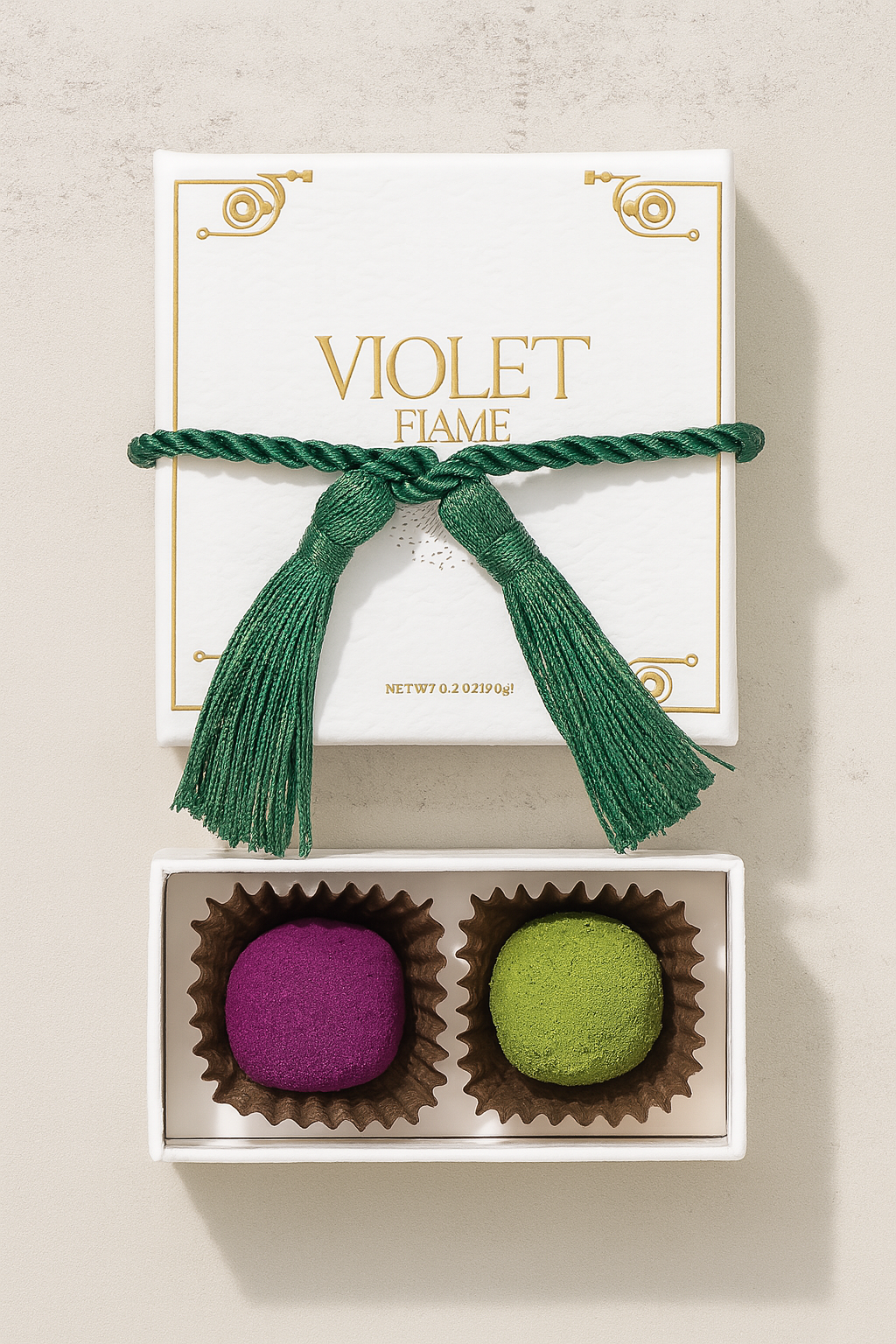 Two colorful chocolate truffles with colorful tops in a box with a green ribbon labeled Violet Flame on a beige background.