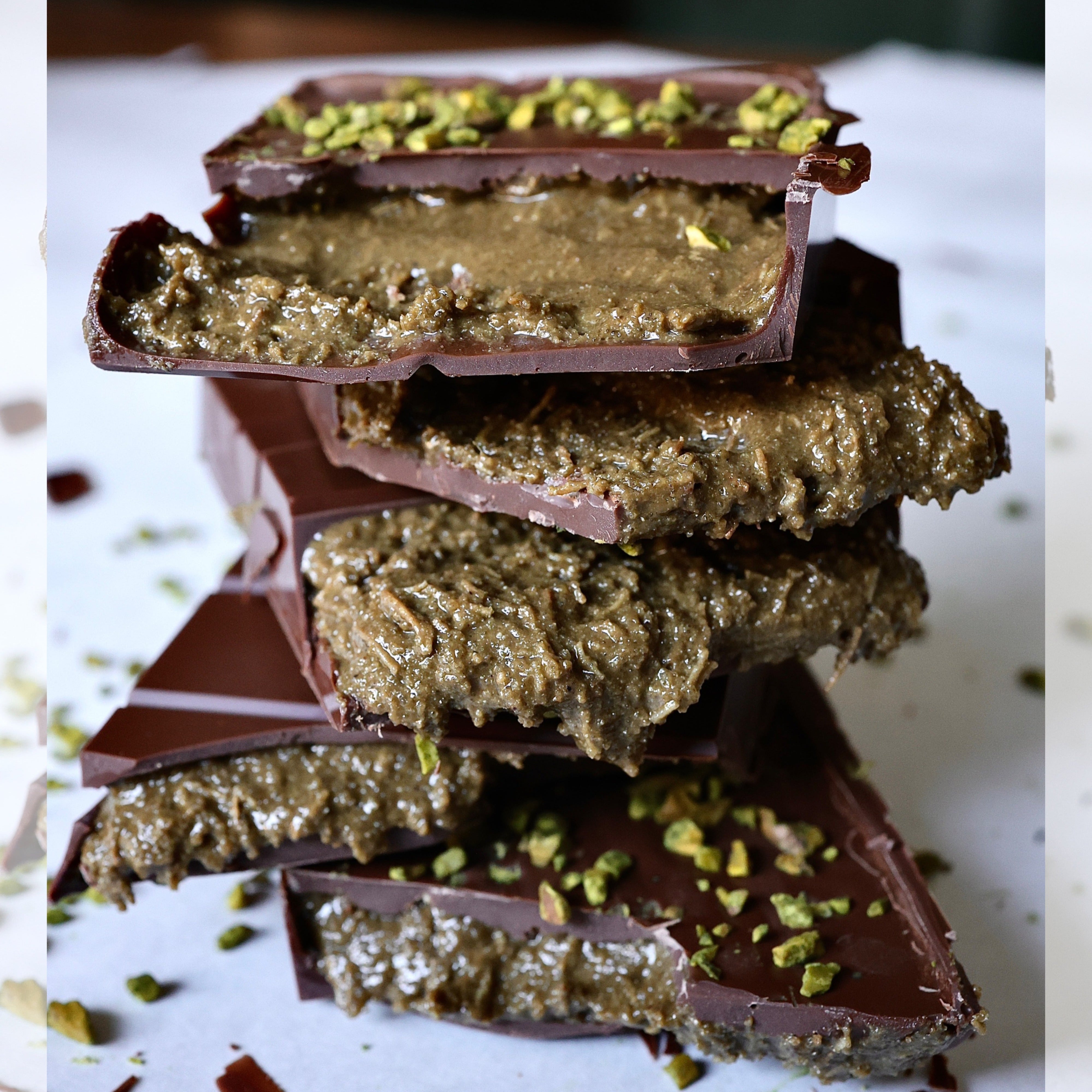 Pieces of Dark Chocolate bars stacked on top of each other topped with crumbled bronte pistachios