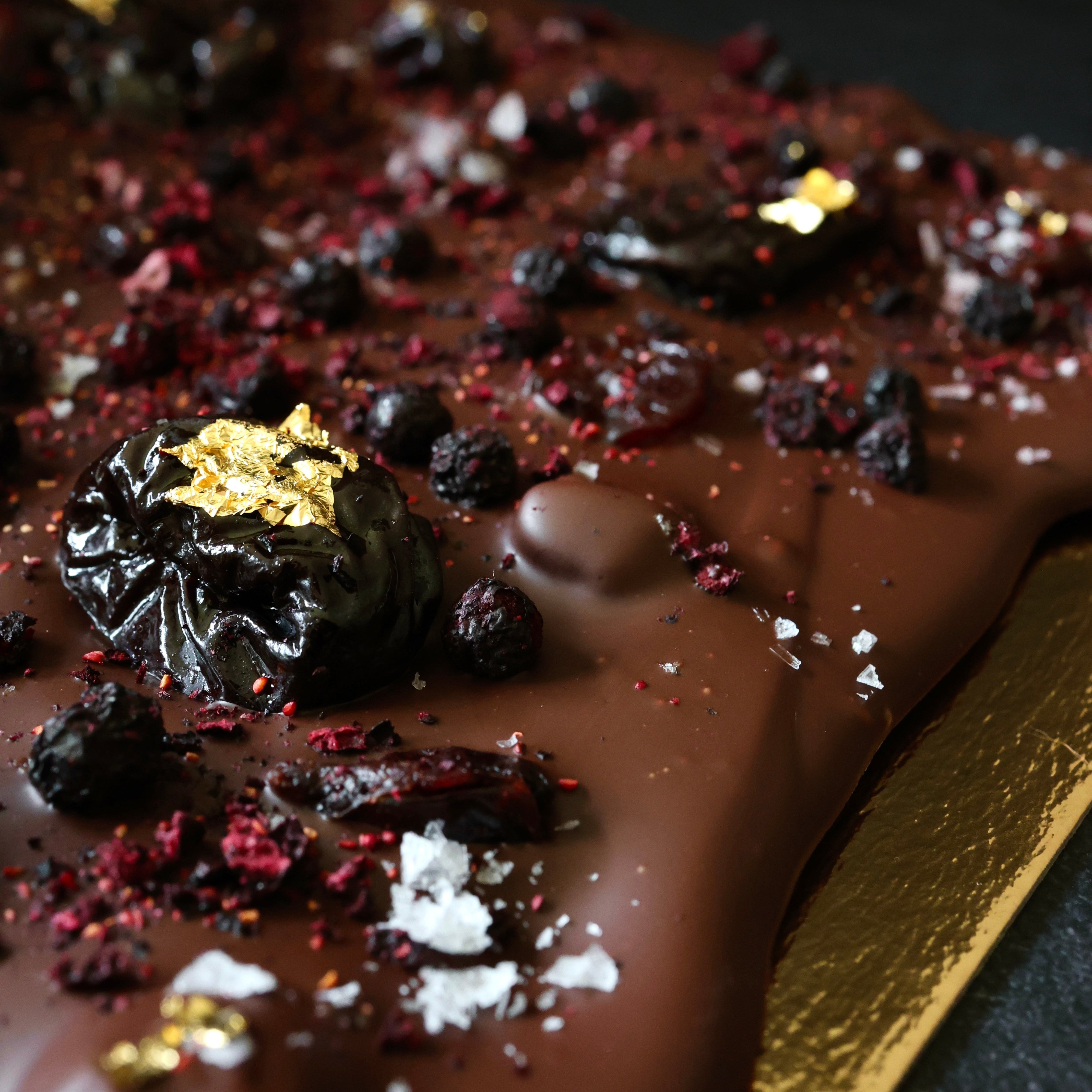 Chocolate bar with dried fruits and gold flakes on a dark background