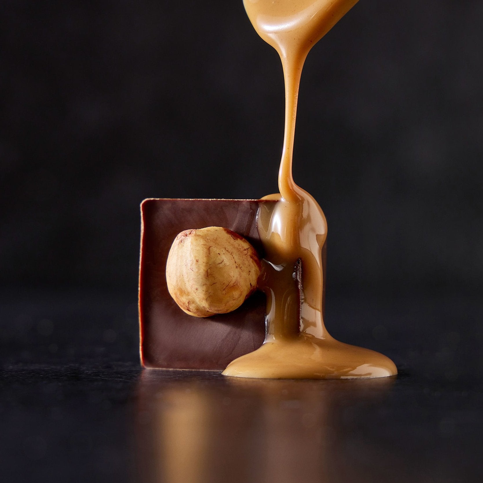 A piece of gianduia chocolate with a whole hazelnut on top, being drizzled with caramel.
