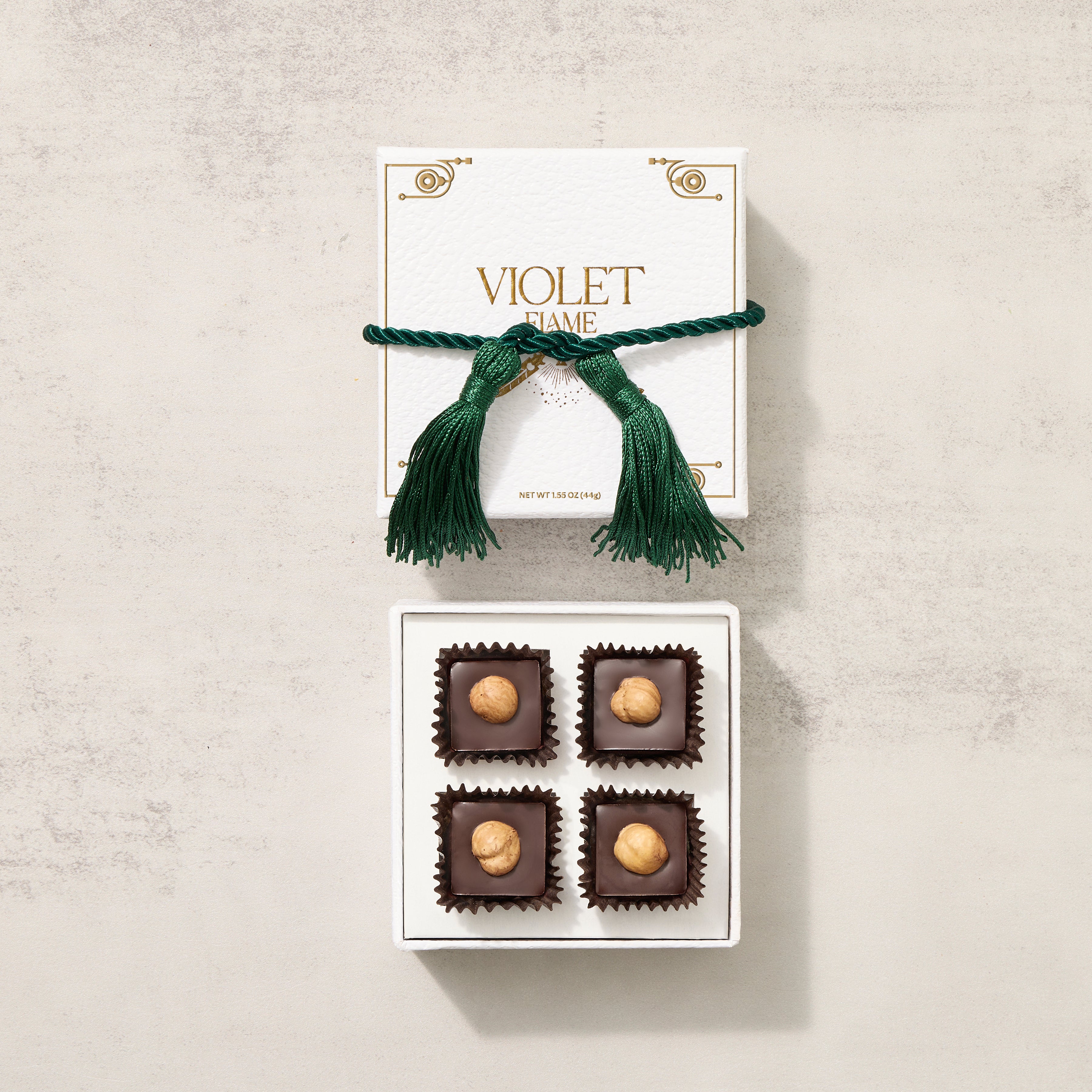 A gift box of Violet Flame gianduia chocolates with a green ribbon on top, displaying four chocolate pieces with hazelnuts.