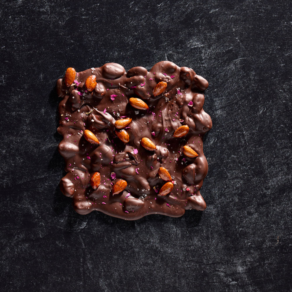 Dark chocolate with smoked almonds on top, presented on a textured dark background.