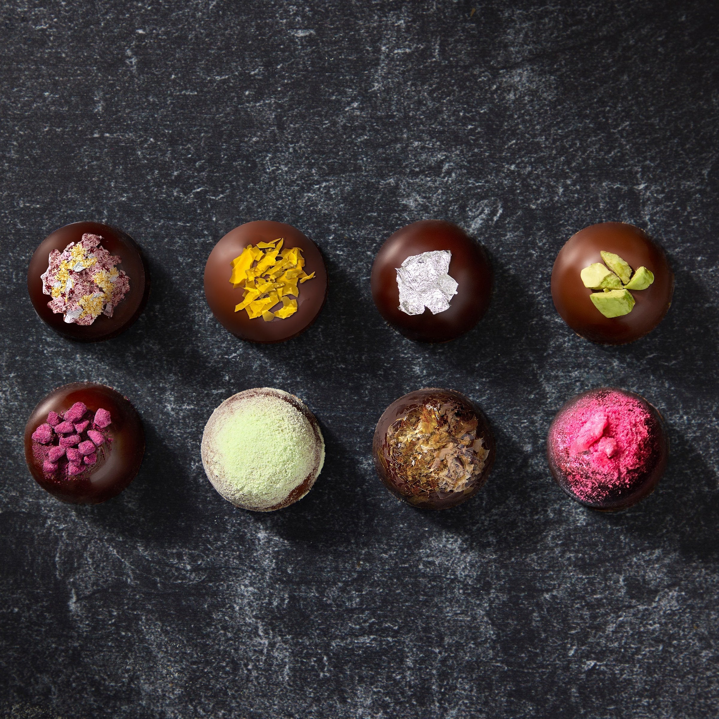 Assorted Milk Chocolate Truffles and Dark Chocolate Truffles topped with bright ingredients including pistachio, raspberry, ube cacao nibs and a silver leaf.