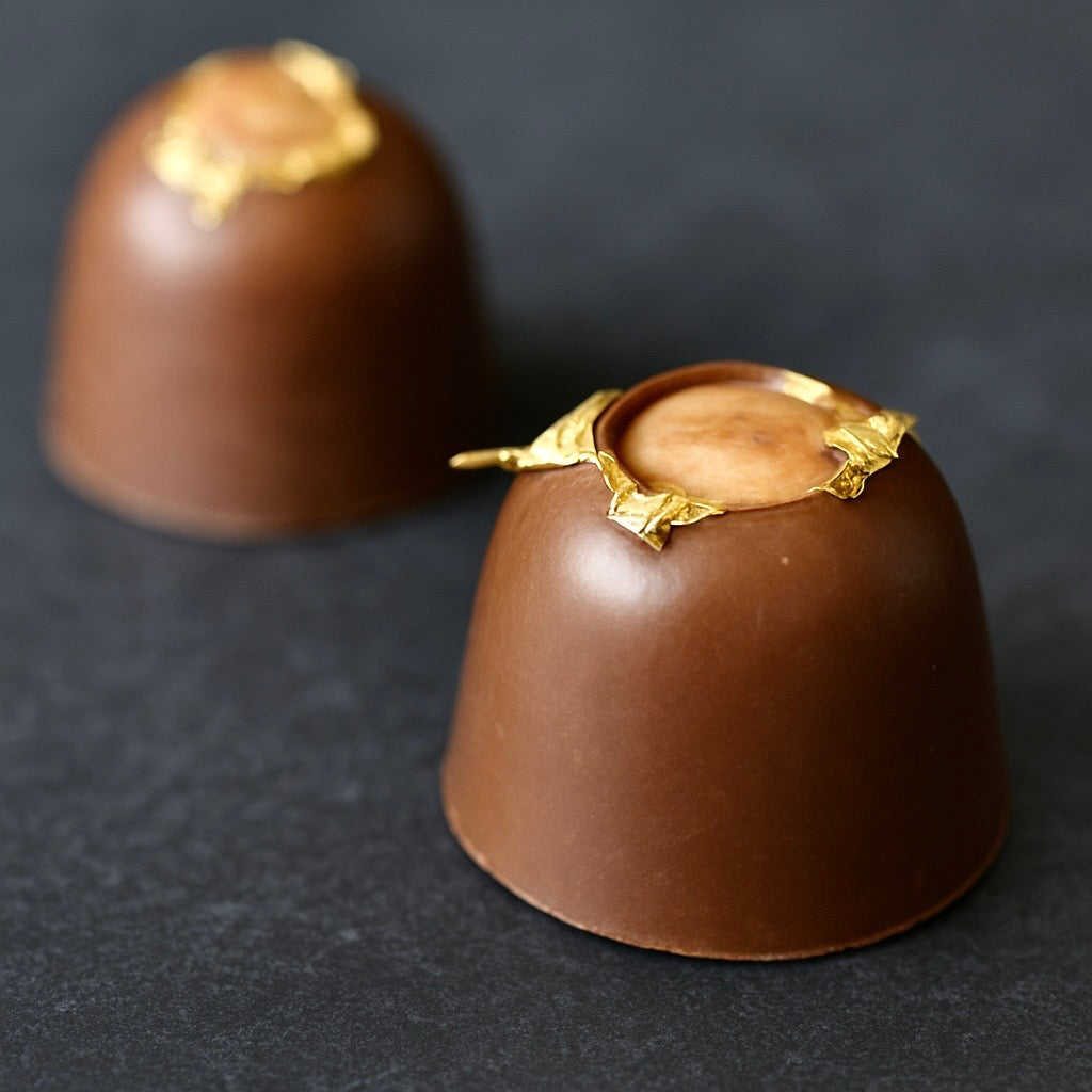 Two hazelnut chocolate truffles with gold leaf on a dark background