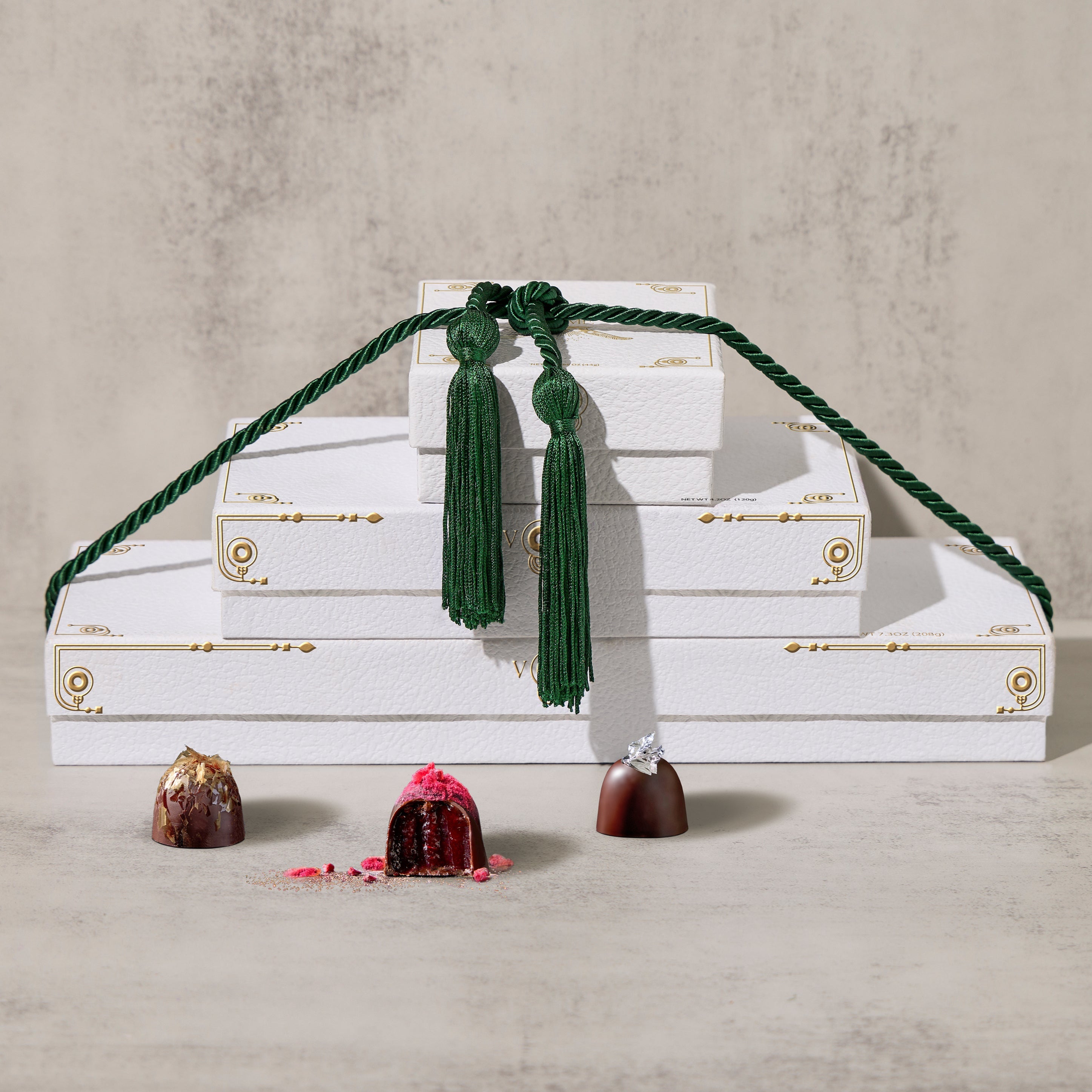 A luxurious chocolate gift set with an assortment of truffles and toffee pieces, neatly arranged in a box with elegant forest green wrapping and a tassel.